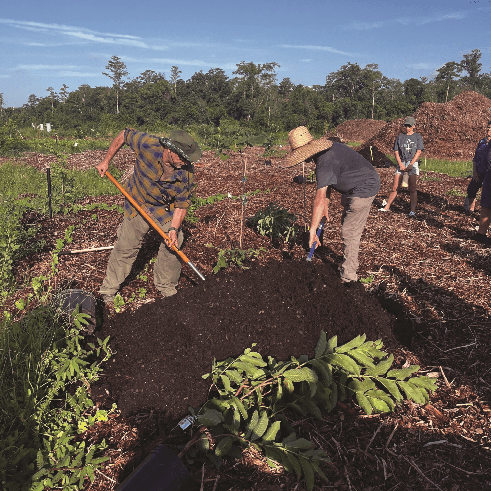 Two men with gardening tools bent over a mound of soil on the 4Rivers campus.