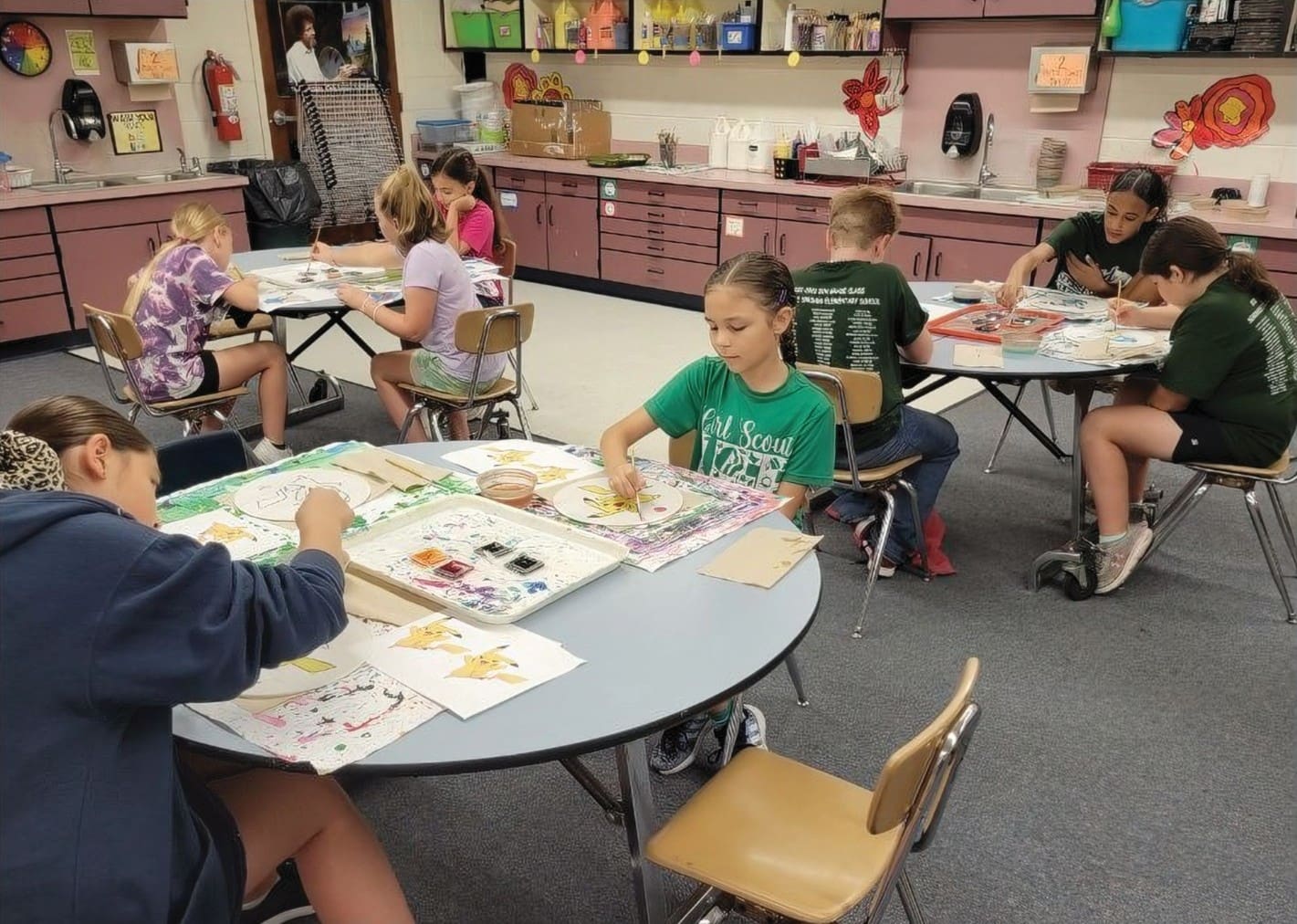 Children sit at tables to do artwork in class.