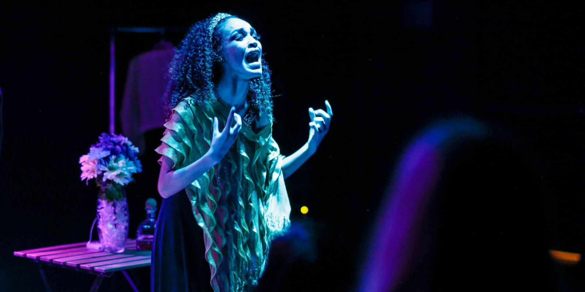 Female performer singing with passion under blue and purple lights. From the Open Scene performance of The Singer Returns.
